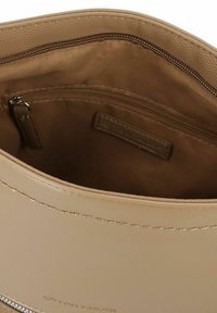 Bolso de hombro beige con exterior de faux leather suave, acentos cosidos y un interior forrado de tela marrón que incluye un bolsillo con cremallera.