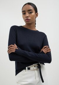 Maglione lavorato a maglia blu navy con maniche lunghe, scollo rotondo e polsini a costine. Abbinato a jeans bianchi e una cintura nera con fibbia dorata.