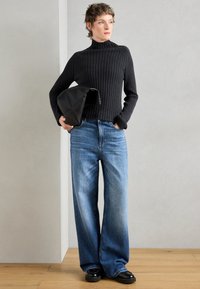 Čierny rebrovaný rolák kombinovaný so svetlo modrými širokými džínsami. Outfit dopĺňa čierny kabelka a robustné čierne topánky.