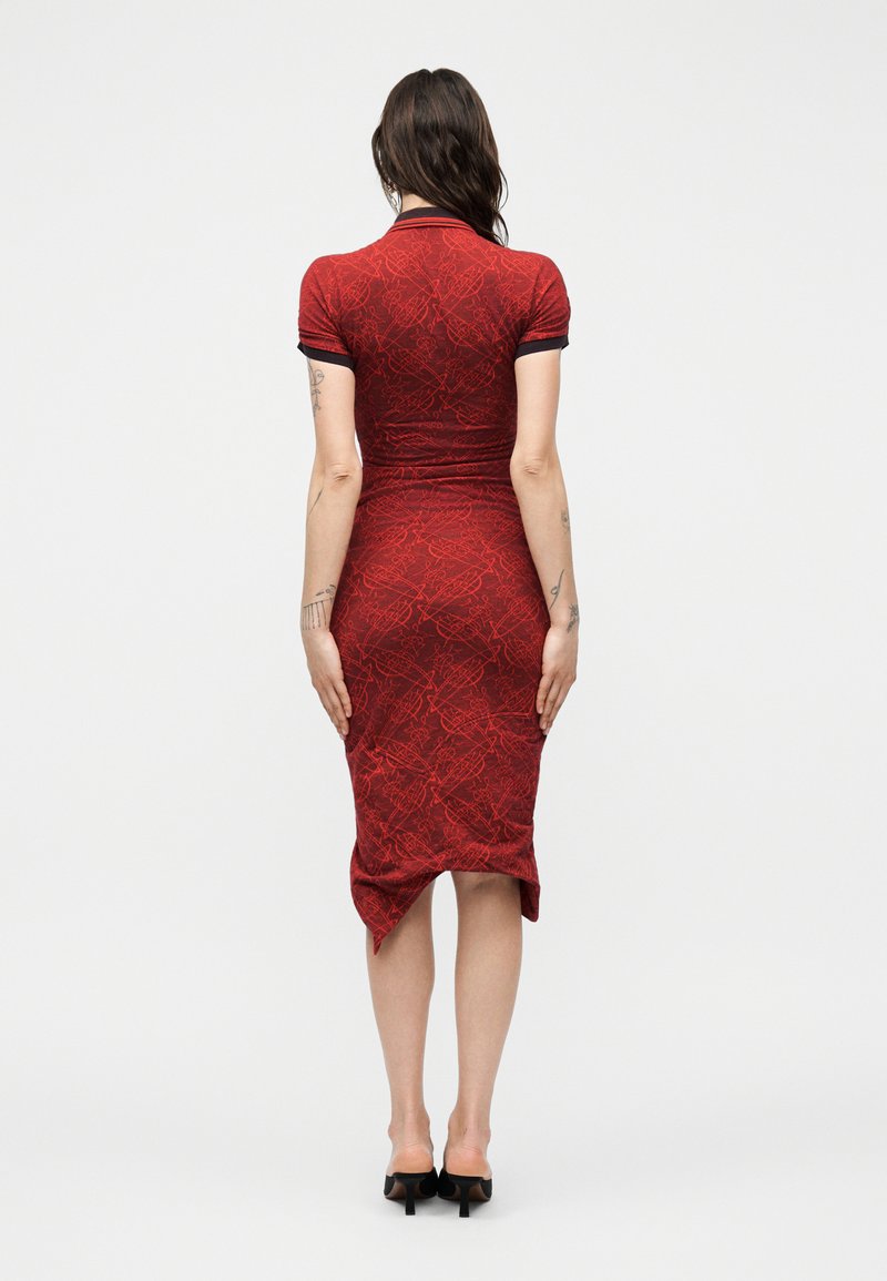 Woman with long dark hair wearing a fitted red patterned midi dress and black heels, standing facing away on a plain white background.