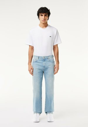White cotton t-shirt with a small logo, paired with light blue denim jeans and white sneakers. Straight-leg design with subtle fading.
