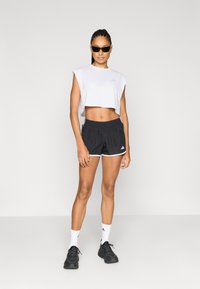 Λευκό cropped τοπ και μαύρο σορτς με λευκές λεπτομέρειες, συνδυασμένα με μαύρα αθλητικά παπούτσια και λευκές κάλτσες, σε αθλητικό στυλ.