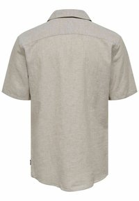 Camisa de manga corta color beige claro, confeccionada en una tela texturizada. Presenta un cuello con solapa y un dobladillo curvado con un acabado sutil y suave.
