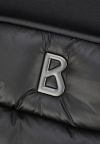 Čierny podšitý materiál s hladkou textúrou obsahuje výrazné šedé písmeno "B" ako dizajnový akcent.