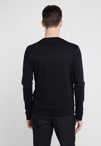 Czarna bluza z długim rękawem i okrągłym dekoltem, o gładkiej fakturze, z prążkowanymi mankietami i wykończeniem na dole. Minimalistyczny design, bez widocznych logo ani wzorów.