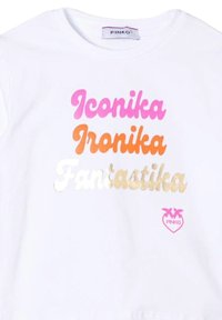 T-shirt bianca in cotone con tre righe di testo: "Iconika" in rosa, "Ironika" in arancione e "Fantastika" in oro. Presenta un piccolo logo rosa.