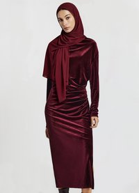 Burgunderfarbenes Samtkleid mit langen Ärmeln, Raffung und seitlichem Schlitz. Kombiniert mit einem passenden burgunderfarbenen Hijab. Glatte Textur.