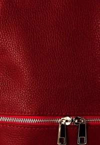 Sac en cuir texturé rouge avec une fermeture éclair en métal argenté en bas, équipé de deux tirettes de fermeture en métal et de coutures contrastantes.