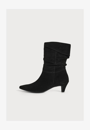 Schwarzer Wildleder-Stiefel bis zur Mitte der Wade mit spitzer Zehe, lockerem Schaft, umgeschlagenem Schaft und niedrigem Kittenabsatz auf weißem Hintergrund.