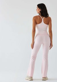 Jasnoróżowy sportowy top z krzyżującymi się ramiączkami, zestawiony z dopasowanymi, rozkloszowanymi spodniami o gładkiej fakturze i minimalistycznym wzornictwie.