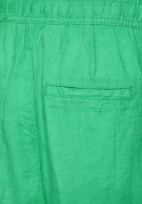 Green linen shorts with an elastic waistband and a single back pocket featuring a stitched rectangular outline. Soft, breathable texture.