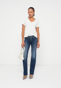 T-shirt blanc à col en V, jeans droit bleu marine, escarpins gris à bouts pointus et un petit sac à main blanc. Design simple avec un minimum de détails.