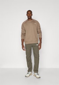 Beige sweater met geribbelde manchetten en ronde halslijn, gecombineerd met olijfgroene cargobroek met zakken. Lichte sneakers maken de look compleet.