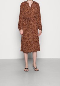 Abito midi marrone con stampa leopardata, scollatura a V, maniche lunghe a sbuffo e vita legata. Abbinato a ciabatte nere.