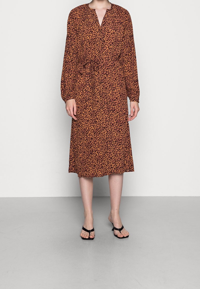 Abito midi marrone con stampa leopardata, scollatura a V, maniche lunghe a sbuffo e vita legata. Abbinato a ciabatte nere.