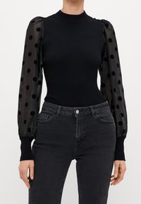 Top aderente nero con maniche lunghe trasparenti caratterizzate da grandi pois neri abbinato a jeans grigi scuri a vita alta.