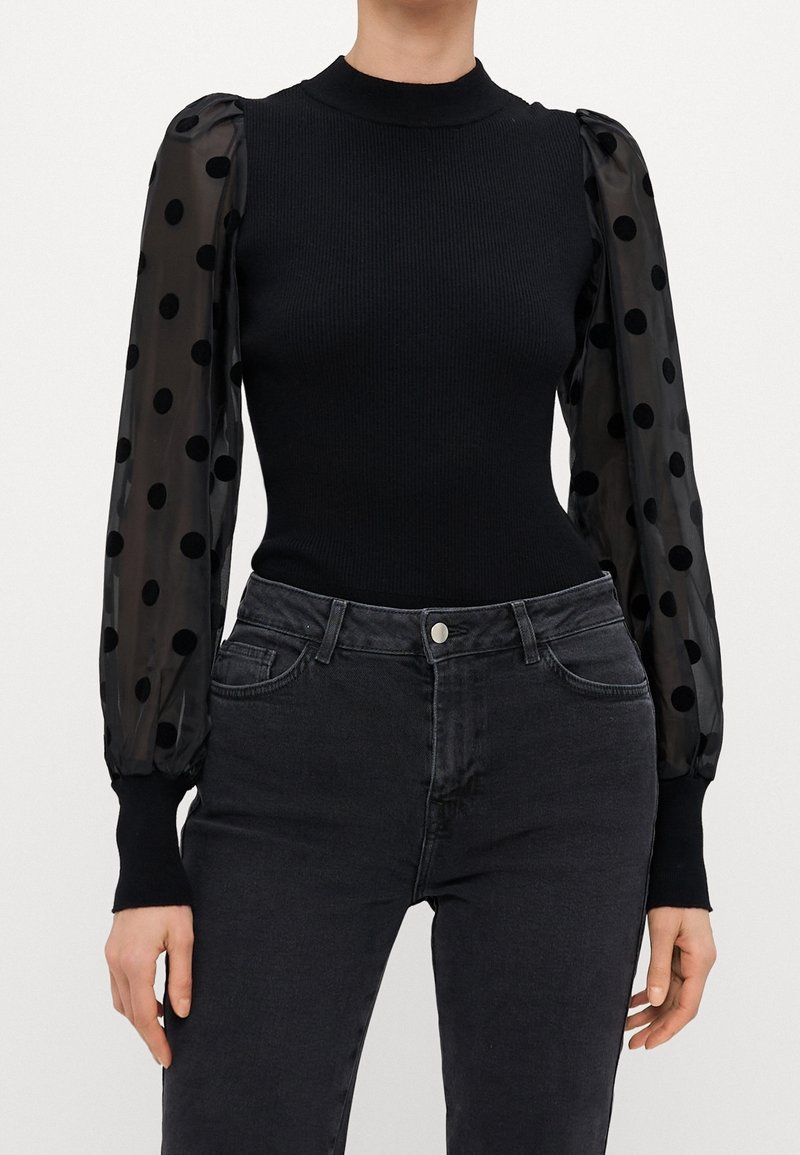 Top aderente nero con maniche lunghe trasparenti caratterizzate da grandi pois neri abbinato a jeans grigi scuri a vita alta.