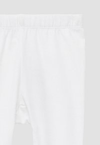 Pantaloni con vita elastica bianca mostrati dalla vita a metà coscia su uno sfondo grigio chiaro.