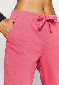 Die rosa Jogginghose hat einen elastischen Bund mit Kordelzug, seitliche Taschen und ein weiches, strukturiertes Material.
