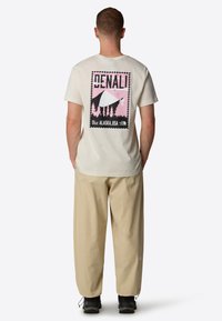 Krémové bavlněné tričko s růžovou a černou grafikou hor a stromů, na zadní straně s nápisem "DENALI, ALASKA, USA".