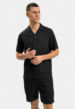 Sort kortærmet skjorte med krave og frontknapper, parret med matchende sorte shorts. Stoffet virker let og glat.