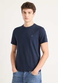 Tricou din bumbac, cu mânecă scurtă, de culoare albastru marin, cu guler rotund și un mic logo pe partea stângă a pieptului. Croială casual, textură netedă.