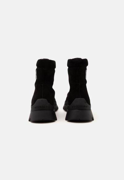 Paire de bottines noires en daim avec semelles épaisses et doublure en fourrure, vues de dos sur un fond clair uni.