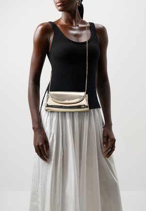 Srebrna metaliczna torebka crossbody z zaokrągloną klapą, łańcuszkowym paskiem i eleganckim prostokątnym kształtem, połączona z czarnym topem bez rękawów i białą spódnicą.