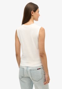 Top sin mangas blanco con escote redondo, hecho de una tela suave, combinado con jeans de mezclilla azul claros que tienen bolsillos traseros y logo.