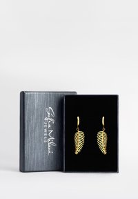Orecchini a forma di foglia d'oro esposti in una scatola foderata di velluto nero; la scatola presenta un logo argentato su un esterno grigio testurizzato.