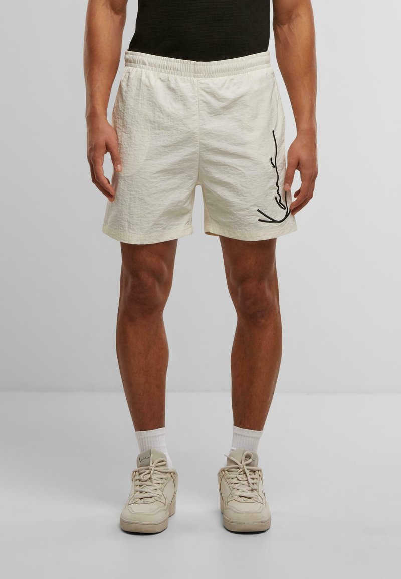 Shorts de couleur crème clair en tissu texturé avec une taille élastique, présentant un dessin en ligne noire sur le côté.