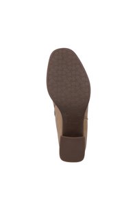 Zapato marrón con suela de goma texturizada, que presenta una punta redondeada y un tacón bajo y grueso, diseñado para la comodidad y la estabilidad.