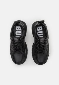 Les baskets en cuir noir présentent une pointe arrondie, un design à lacets, une surface texturée et un logo de marque bien visible sur les semelles intérieures.