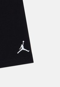 Čierne bavlnené tričko s bielym logom Jumpman na dolnom ľavom boku, s hladkou textúrou a štandardným strihom.