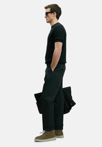 Zwarte geribbelde shirt met korte mouwen, zwarte tapered broek, tan suède laarzen, houdend een zwarte jas. Schone lijnen en een op maat gemaakte pasvorm.