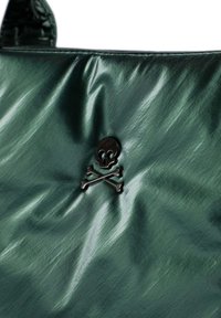Bolso verde brillante con un emblema central de calavera y huesos cruzados en negro, con una textura arrugada y material suave.