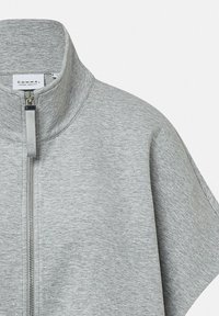 Maglione grigio a maniche corte con zip, realizzato in tessuto morbido, dotato di un colletto alto e di una cerniera metallica con un tirante in tessuto. Etichetta del marchio visibile.