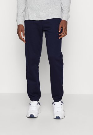 Granatowe spodnie dresowe wykonane z miękkiego materiału z elastycznymi mankietami, zestawione z białymi trampkami z ciemnymi akcentami i sznurowadłami.