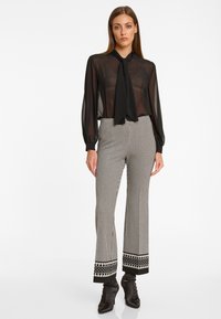 Schwarze transparente Bluse mit einer Krawattenkragen, kombiniert mit hoch taillierten, houndstooth-musternden Hosen, die am Saum eine dekorative schwarze Borte aufweisen.