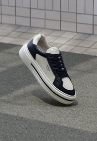 Valged ja tumesinised nahast tossud perforeritud varvastega, shoelaces ja tekstureeritud kummitald, millel on brändimine külgedel.