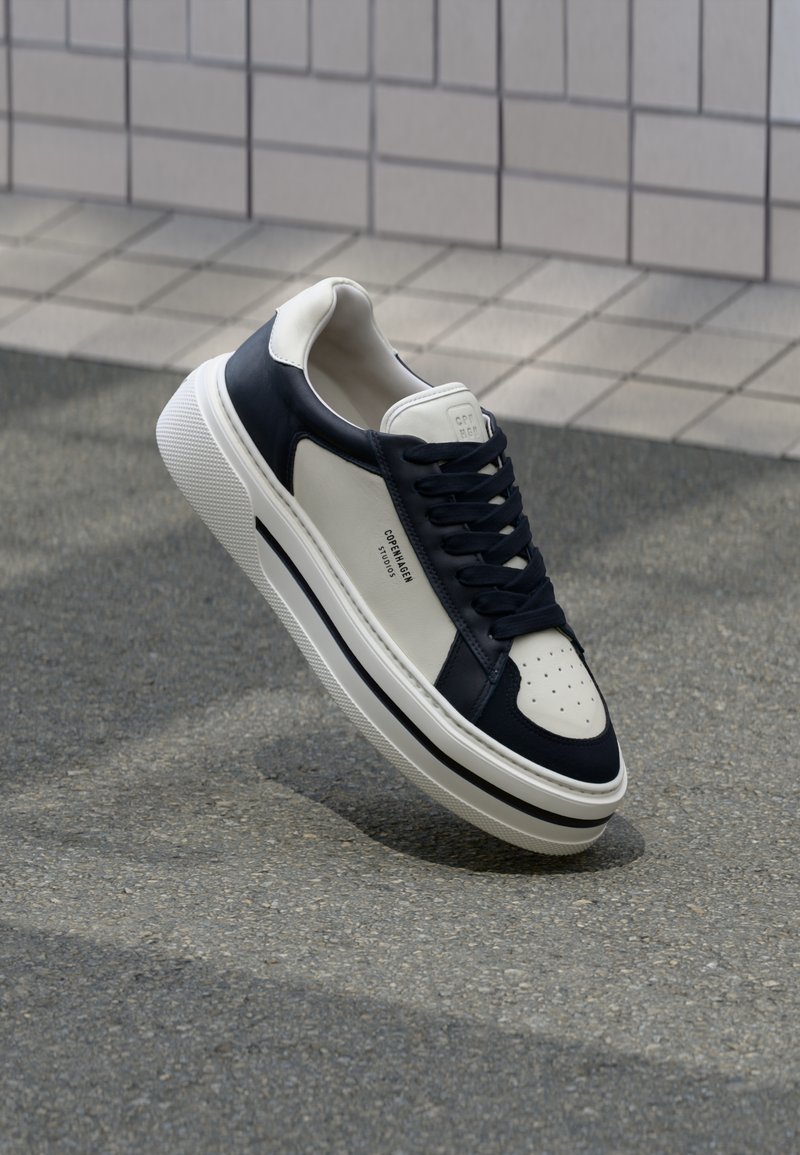 Valged ja tumesinised nahast tossud perforeritud varvastega, shoelaces ja tekstureeritud kummitald, millel on brändimine külgedel.