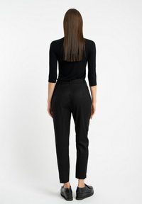 Czarna dopasowana bluzka z trzema ćwierć rękawami, w połączeniu z czarnymi spodniami o wysokim stanie i zwężającymi się nogawkami oraz czarnymi butami na platformie.