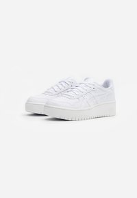 White athletic sneakers with a textured upper, perforated detailing, flat laces, and a thick, ridged sole. Minimalistic design.