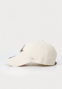 Beige bomullsmössa med böjd skärm, utrustad med bruna broderade accenter och en liten logotyp på sidan. Texturerad tyg med sömsdetaljer.