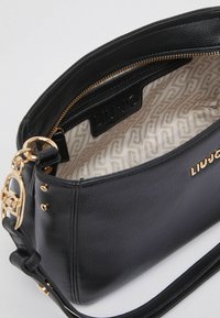 Sac à main en cuir noir à la finition texturée, avec des éléments en métal doré et un intérieur à motif. Dispose d'une fermeture éclair et d'une bandoulière réglable.