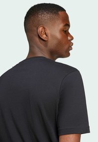 Camiseta negra de manga corta hecha de suave tela de algodón; presenta un clásico cuello redondo y una textura lisa con un mínimo de detalles.