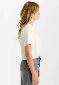 T-shirt blanc court à manches courtes et encolure ronde, associé à un jean en denim gris taille haute avec un design de poche arrière.