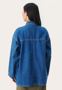 Farmerdzseki, kék, laza szabás, hosszú ujjú, hegyes gallér, látható varrási részletek, enyhén oversized, lekerekített szegély.