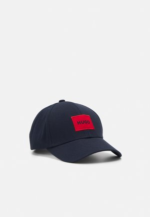 Casquette de baseball bleu marine avec une visière incurvée et un patch rectangulaire rouge portant l'inscription "HUGO" au centre avant.