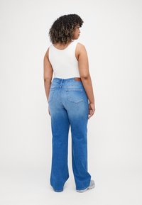 High-waisted blue denim jeans with a slight fade, straight-leg cut, two back pockets, and a contrasting brown belt loop detail.